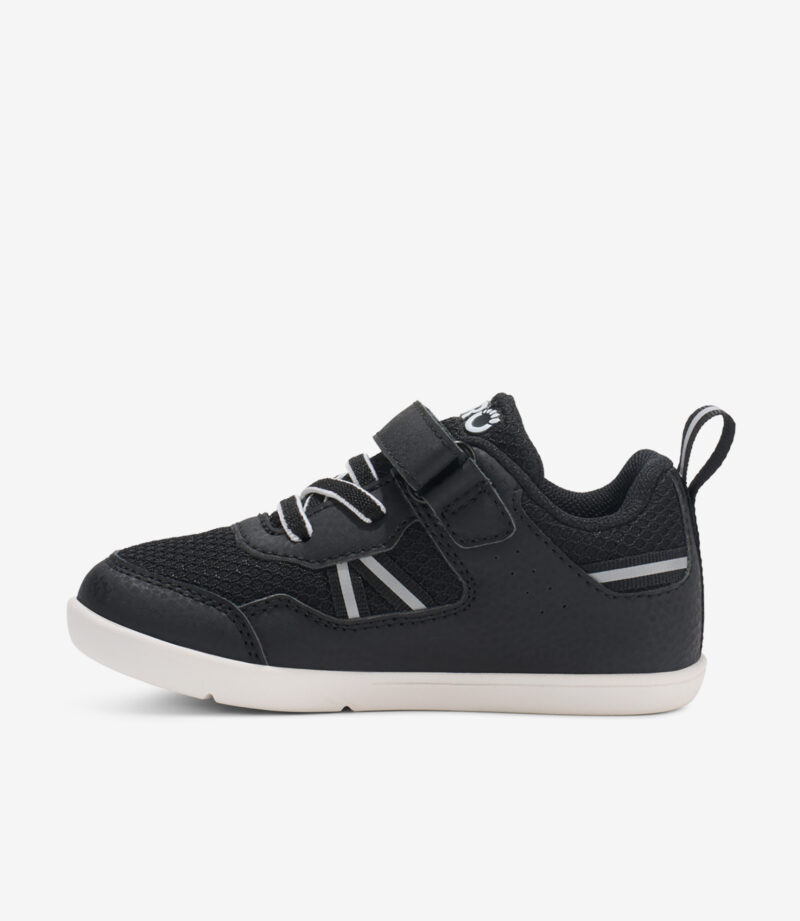 Sort-hvide barfodssko til børn med velcro, elastiske snørebånd, bred tåboks, minimalistisk gummisål, set fra siden.