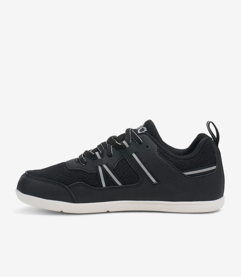 Sort og hvid barfodssko til børn, overdel i mesh, bred tåboks, minimalistisk sneaker-stil med perforerede sider på hvid baggrund.