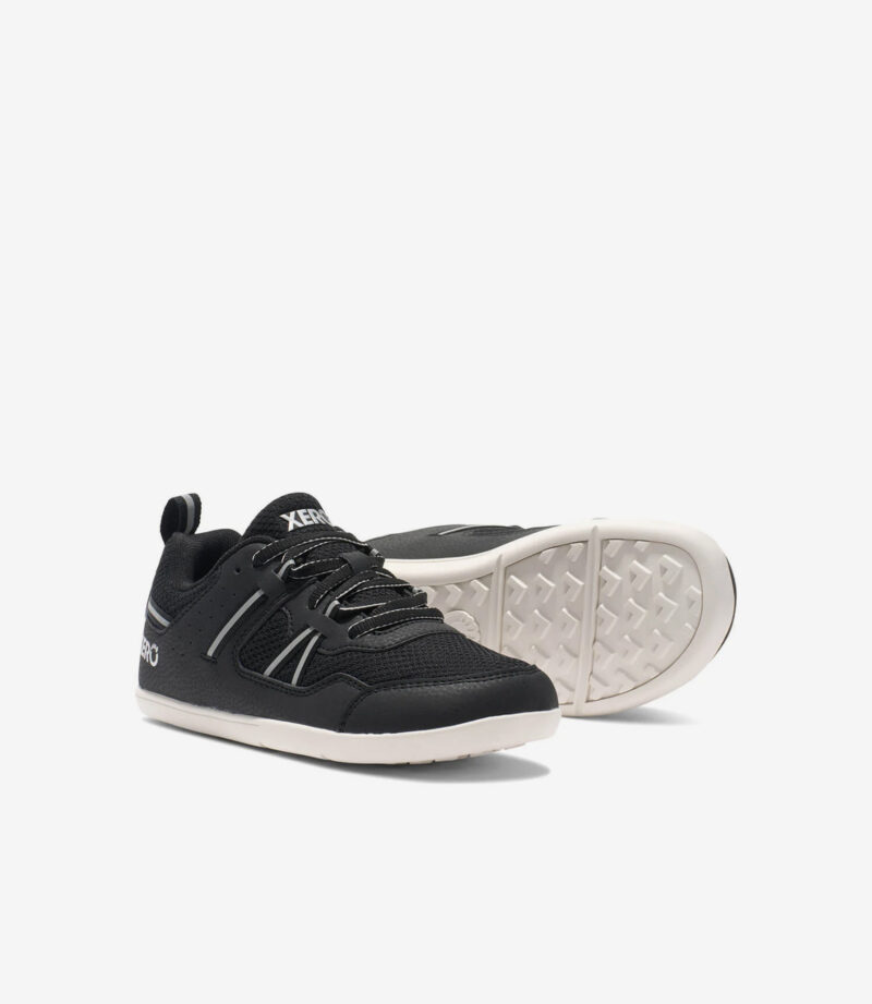 Sorte og hvide Xero Prio børn barfodssneakers, bred tåboks, minimalistisk design, fleksibel sål vist fra siden og trædefladen.